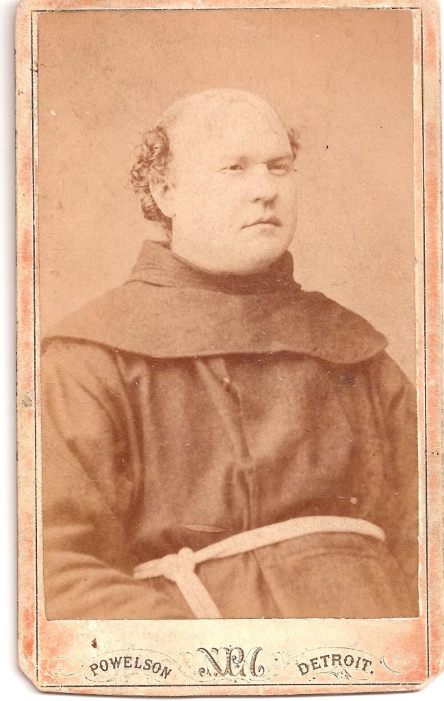 A younger photograph of Bonaventure Hammer (1842-1917). He has a bald pate, with hair around the ears. He wears a monk's robes with a corded sash. Beneath the photograph is the photographer's name: Powelson, the letters N P A, and Detroit.